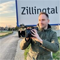 Georg Csarmann mit Filmkamera vor dem Ortsschild Zillingtal