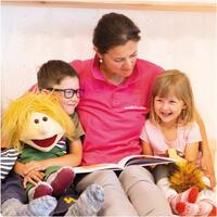 Notfallmama von KiB children care liest zwei Kindern mit einer Handpuppe aus einem Bilderbuch vor